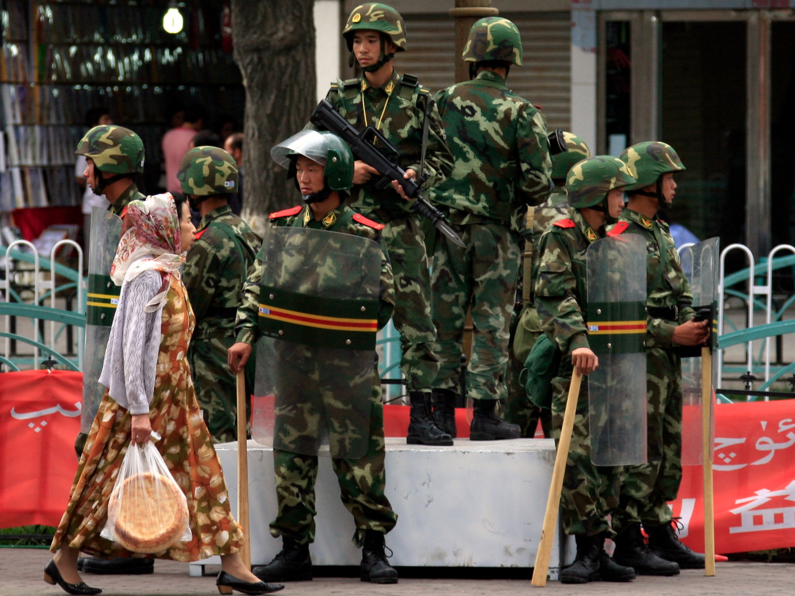    Ethnic Uyghur woman walks past armed Chinese paramilitary police in riot gear in Xinjiang (File Photo/ Reuters)