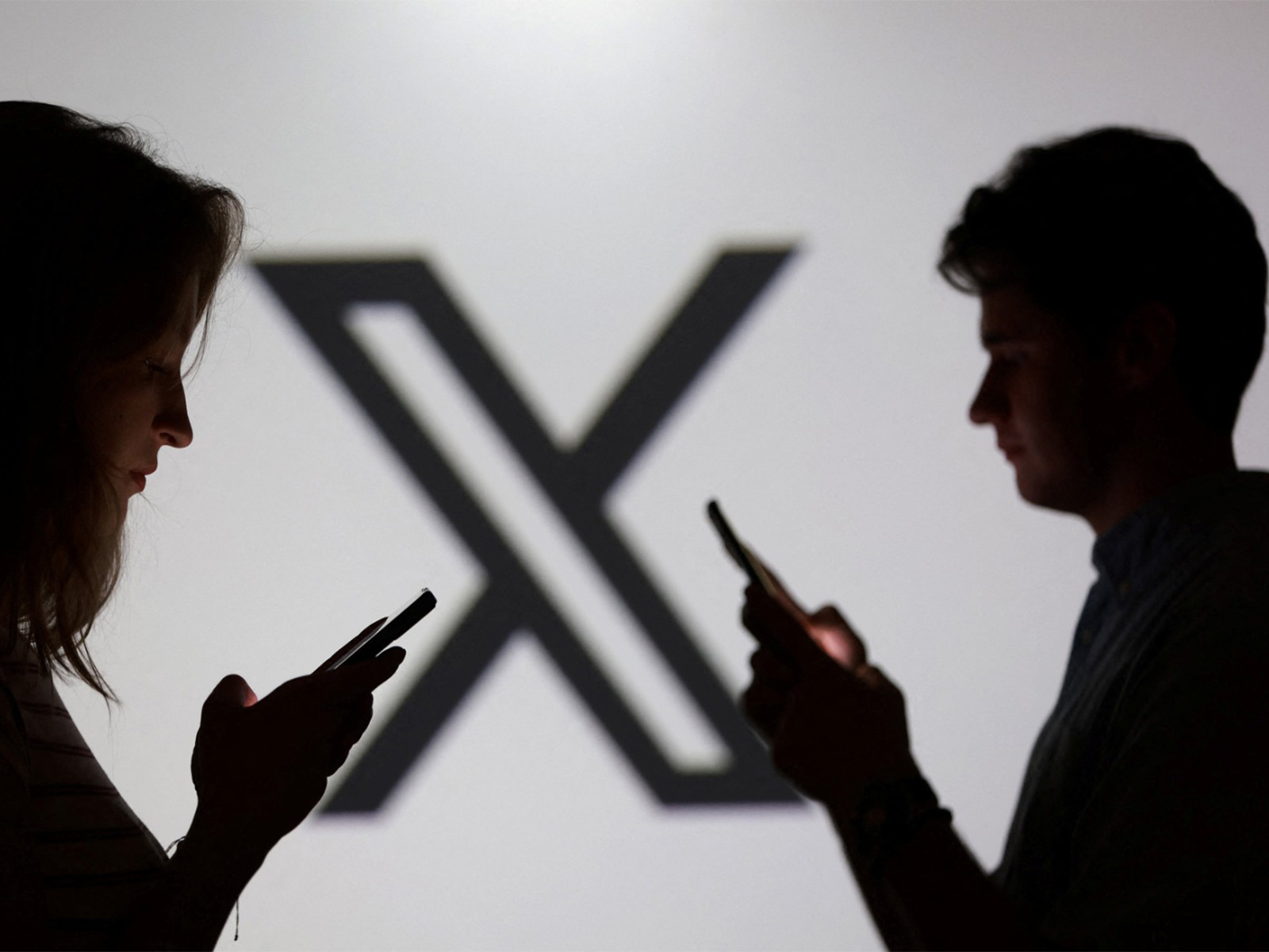 Teenagers pose for a photo while holding smartphones in front of a X logo (Photo/ Reuters) Teenagers pose for a photo while holding smartphones in front of a X logo (Photo/ Reuters)