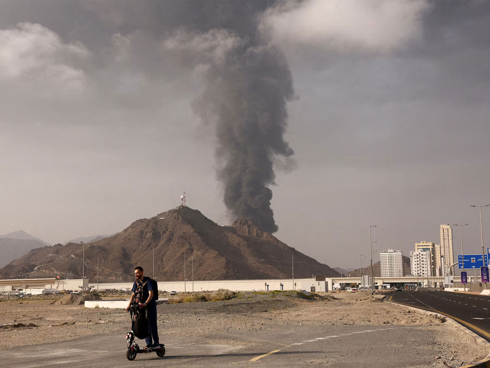 A person rides a scooter as smoke billows from the Fujairah Oil Industry Zone after debris from a drone intercepted by air defences triggered a fire, in Fujairah, United Arab Emirates (File Photo/Reuters)