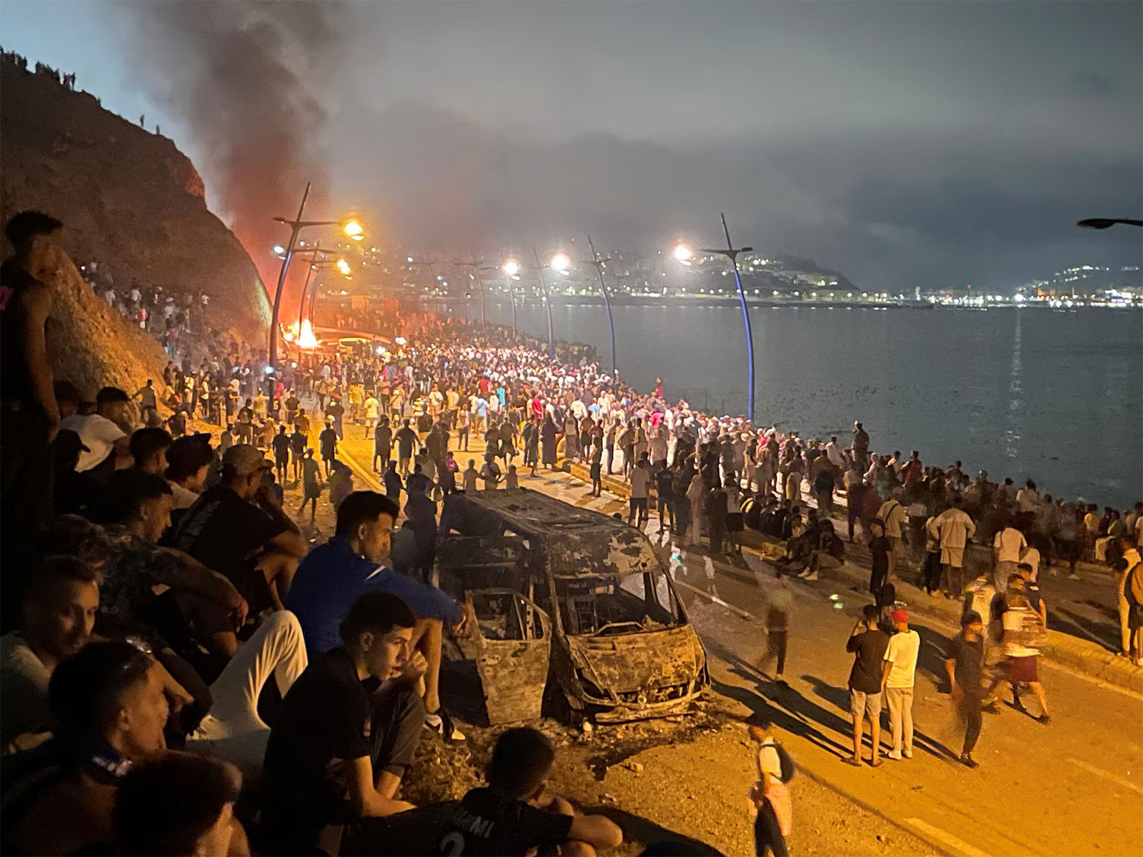 Migrants gather near a burning vehicle on the Moroccan side of the border in Fnideq, awaiting a chance to cross into the Spanish enclave of Ceuta. (Photo/Reuters)