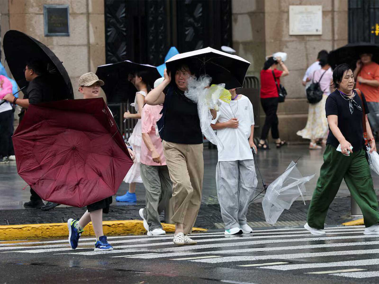 A person carrying a damaged umbrella as pedestrians cross a road amid strengthening winds ahead of Typhoon Dolphin’s arrival in Shanghai, China. (Photo/Reuters)