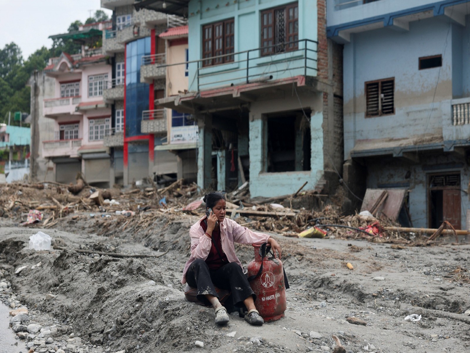 A woman speaks on a phone as she sits next to a gas cylinder at the site of flash floods and mudslides, in Devighat (File Photo/ANI) A woman speaks on a phone as she sits next to a gas cylinder at the site of flash floods and mudslides, in Devighat (File Photo/ANI)