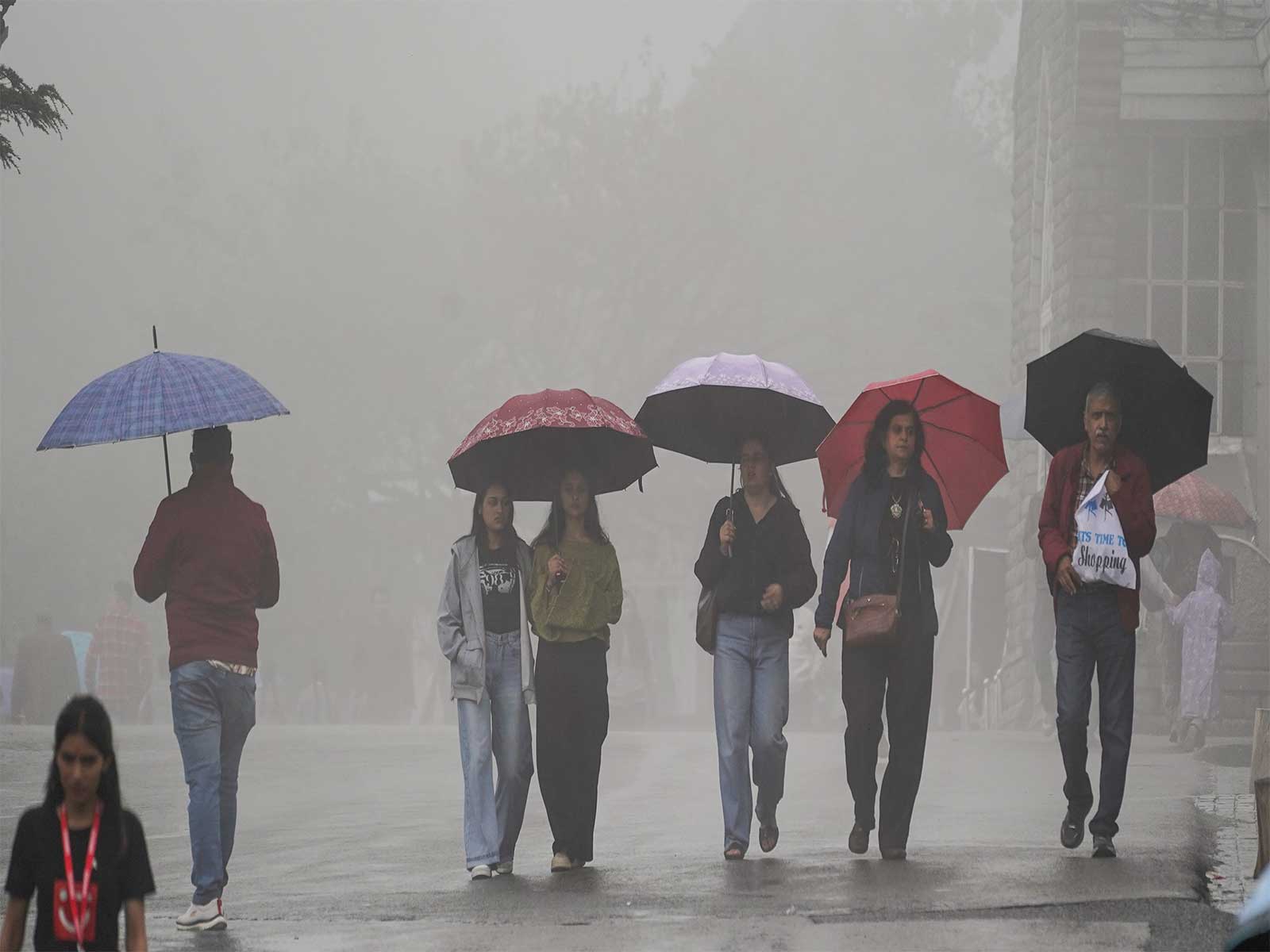 Pedestrians holding umbrellas make their way through rain-slicked roads amid heavy rainfall (File Photo/ANI)
